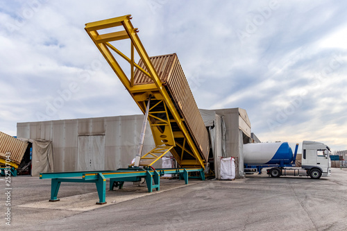 Contenedor descargando levantado sobre plataforma realizando operaciones de trasvase para cargar camión silo cisterna en puerto seco