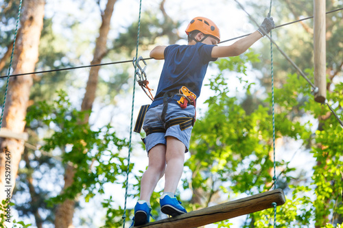 Cute young boy in helmet with climbing equipment in the rope amusement park. Summer camp, holidays concept