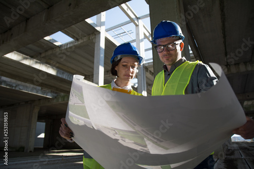 Two young engineers on a construction site, discussing project details