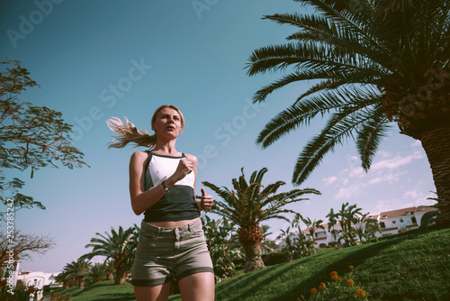 the girl is engaged in morning jogging among palm trees in a respectable suburb area.