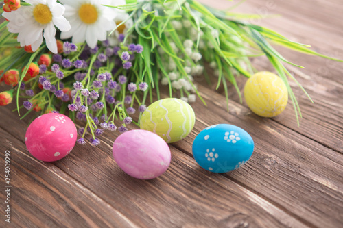 Colorful Easter eggs and spring flowers on rustic wooden background. © Alik Mulikov