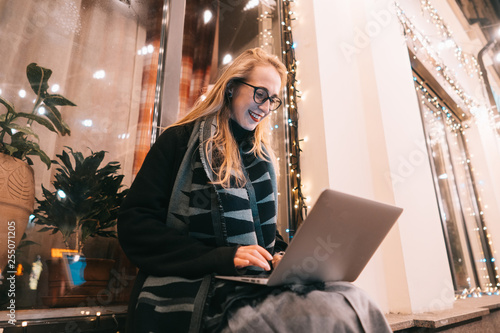 side view of young woman using laptop on street with night city