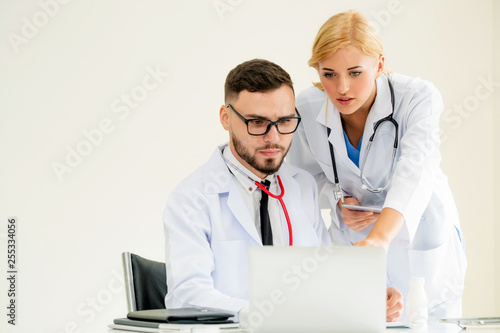 Doctor at hospital office working on laptop computer on the table with another doctor having discussion about patients health.
