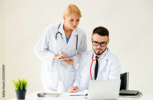 Doctor at hospital office working on laptop computer on the table with another doctor having discussion about patients health.