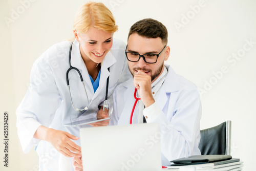 Doctor at hospital office working on laptop computer on the table with another doctor having discussion about patients health.