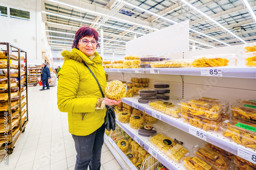 Beautiful mature woman holding a pack of oriental sweets chak-chak. Text in Russian: honey twig, brushwood with sesame