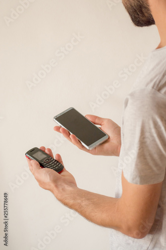 Male hands holding a new smart phone and an old cellphone, on white background. Planned obsolescence concept, technology development, history of communications, millenial devices