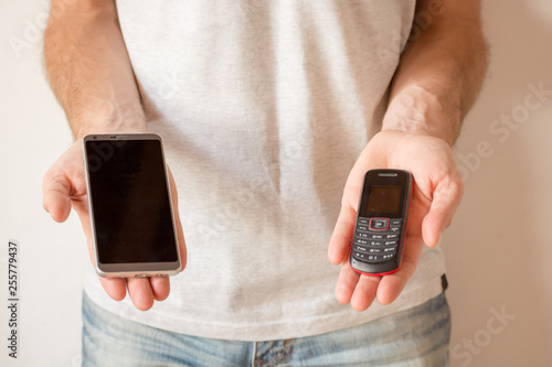 Male hands holding a new smart phone and an old cellphone, on white background. Planned obsolescence concept, technology development, history of communications, millenial devices