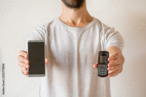 Man holding a new smart phone and an old cellphone, on white background. Planned obsolescence concept, technology development, history of communications, millenial devices