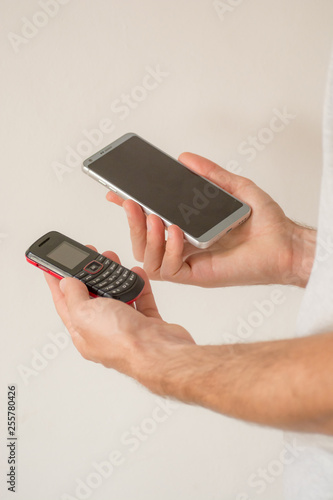 Male hands holding a new smart phone and an old cellphone, on white background. Planned obsolescence concept, technology development, history of communications, millenial devices