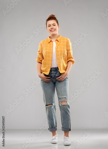people concept - smiling red haired teenage girl in checkered shirt and torn jeans over grey background © Syda Productions