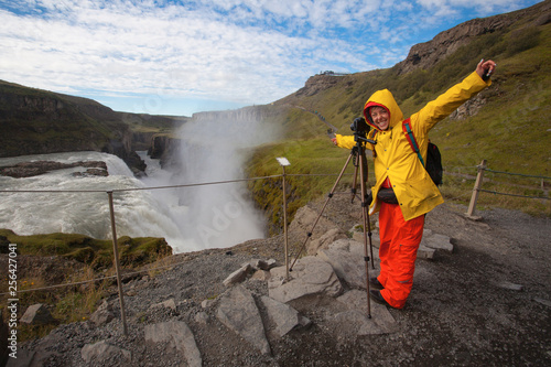 Woman in bright yellow and red clothes making photos in amazing Detifoss waterfall, Iceland