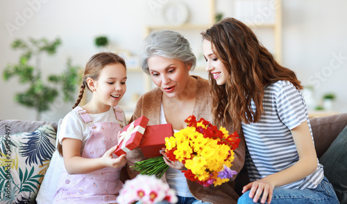 mother's day! three generations of family mother, grandmother and daughter congratulate on the holiday, give flowers . © JenkoAtaman