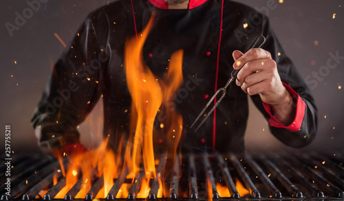 Closeup of chef holding fork above the grill © Jag_cz