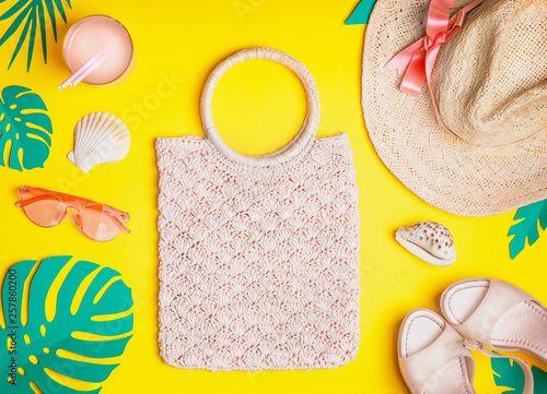 Summer female outfit. Flat lay. Woven hand bag, straw hat, sunglasses, sandals with cocktail , seashells and tropical paper palm leaves on yellow background, top view. Summer holiday vacation. © VICUSCHKA