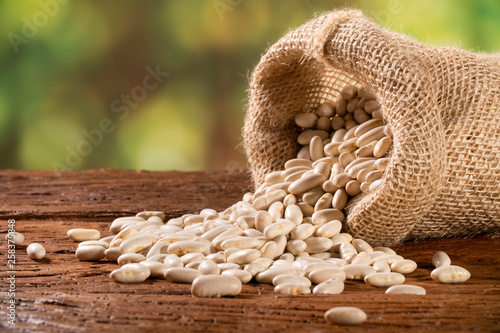 White dried haricot kidney beans in burlap sack on wooden table , heap of legume bean concept. Legumes background © paulovilela