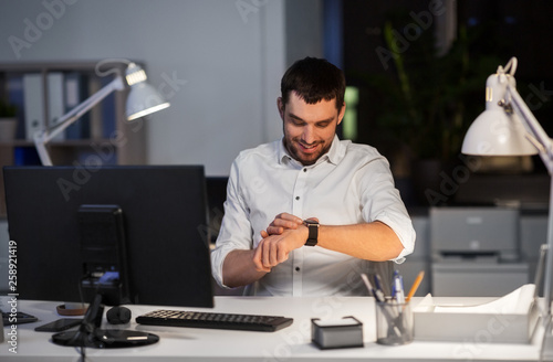 business, technology and time management concept - happy smiling businessman with smart watch at nigh office © Syda Productions