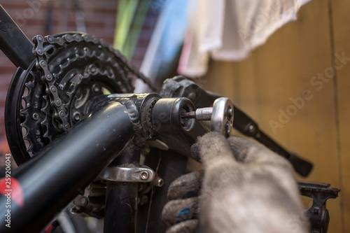 A close-up of a male bicycle mechanic's hand in the workshop uses a screwdriver tool to adjust and repair the bicycle crank assembly, the front bike stars © silentalex88