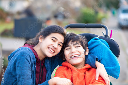Big sister hugging disabled brother in wheelchair outdoors, smiling © Jaren Wicklund