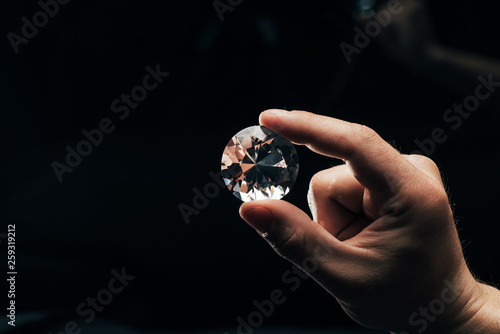 partial view of man holding big clear shiny diamond on black background © LIGHTFIELD STUDIOS