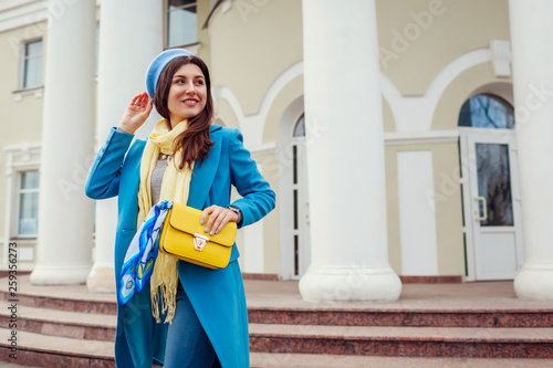 Young woman in trendy blue coat walking in city holding stylish handbag. Spring female clothes and accessories. Fashion © maryviolet