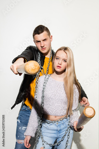 Sport games. Close up fashion portrait of two young cool hipster girl and boy wearing jeans wear. Woman and man with a baseball bats. Studio shot of two cheerful best friends having fun and making © master1305