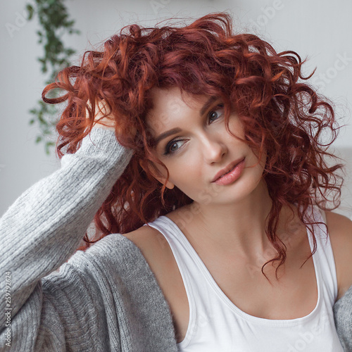 Very attractive young woman indoors. Portrait of curly haired female. Redhaired beautiful woman at home. © olenachukhil