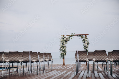 arch for the wedding ceremony and chairs for guests stand on the background of water © alexgukalov