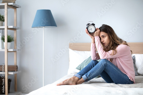 Sad woman holding alarm clock on the bed. © BestForYou
