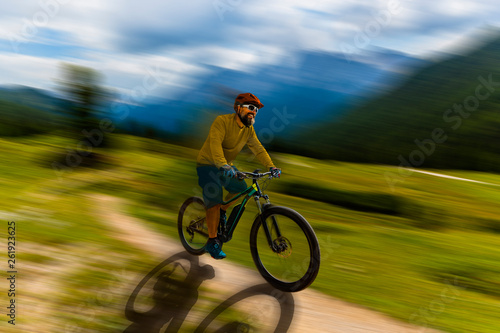 Single mountain bike rider on electric bike, e-mountainbike rides up mountain trail. Man riding on bike in Dolomites mountains landscape. Cycling e-mtb enduro trail track. Outdoor sport activity. © Gorilla