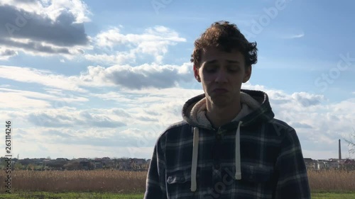 pensive young guy with short curly hair standing on the blue cloudy sky background. Slow motion © DubstepWar