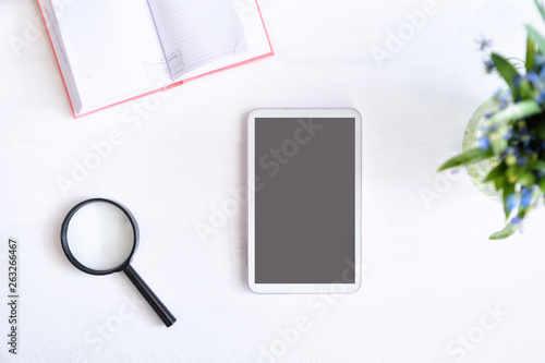 Tablet with black empty screen. Notebook, magnifier and flowers on table © somemeans