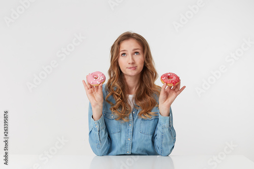 Young beautiful girl holds donuts in her hands, she is dieting, but dreams of eating donuts, imagines what they are tasty and sweet isolated over white background. © timofeiwolny