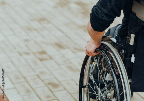 Close-up of male hand on wheel of wheelchair during walk in park © Natalia