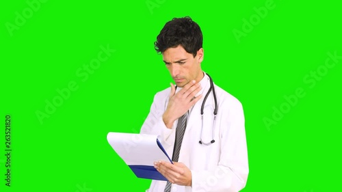 Young doctor reading a case history isolated on green screen chroma key background © Minerva Studio