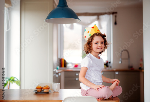 A small girl with a paper crown at home, looking at camera. © Halfpoint