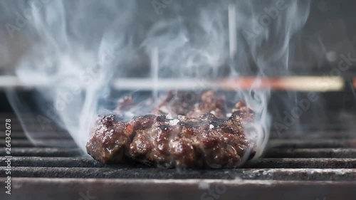 fried juicy meat for the Burger, sprinkle with white salt. lots of smoke. Slow motion. Close up © Goodwyn