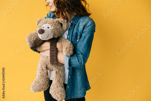 cropped view of redhead girl hugging teddy bear and standing on orange © LIGHTFIELD STUDIOS