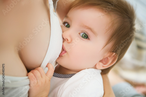 Mother breastfeeding baby in her arms at home. Mom breast feeding her newborn child. Baby eating mother's milk. Concept of lactation infant © Alik Mulikov